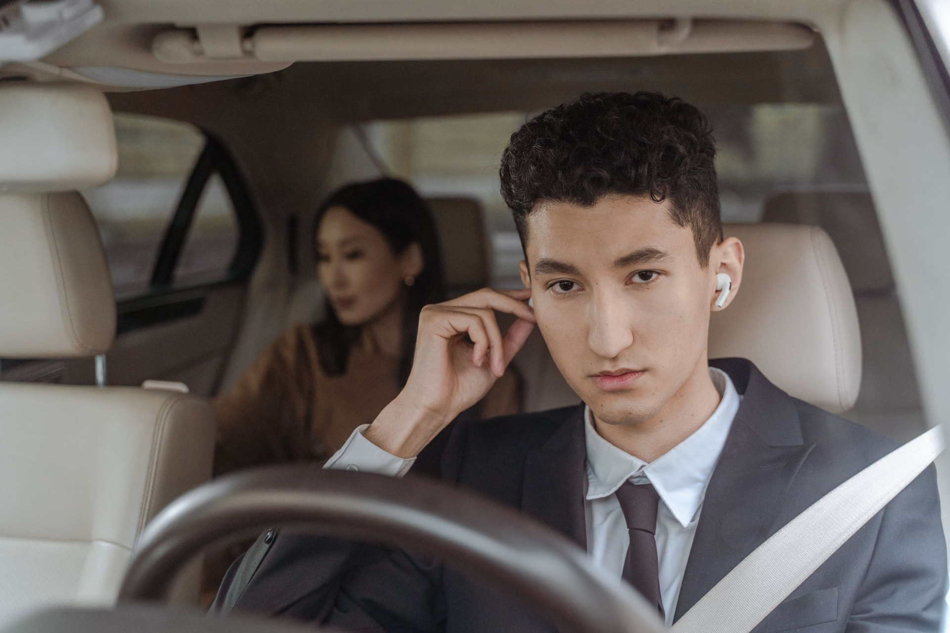 Chauffeur in a dark suit at the wheel of a luxury vehicle with cream leather interior, passenger seated behind
